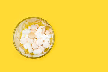 Pastillas y medicamentos dentro de un vaso de cristal sobre un fondo amarillo brillante liso y...