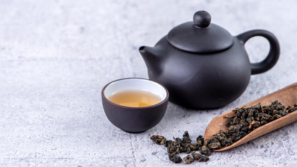 Hot tea in black teapot and cups and dry tea leaves over bright gray cement background, close up, copy space design concept.