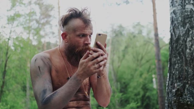 Wild Homo Sapiens with Mustache Holding Mobile Phone and Makes Online Video Translation. He Speaking and Talking and Socializing with People Remotely. Cave Dweller and High Tech Industry.