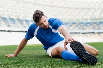 Naklejka premium selective focus of professional soccer player in blue and white uniform stretching on football pitch at stadium