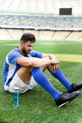 professional soccer player in blue and white uniform sitting on football pitch with sports bottle at stadium © LIGHTFIELD STUDIOS