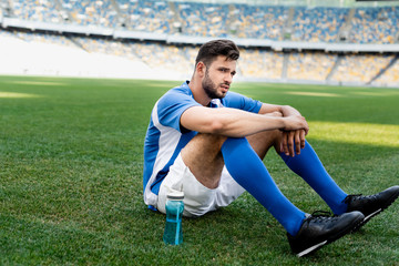 professional soccer player in blue and white uniform sitting on football pitch with sports bottle at stadium © LIGHTFIELD STUDIOS