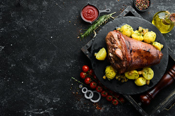 Baked pork leg with potatoes on a black stone plate. Pepper steak. Top view, free space for your text. Rustic style.