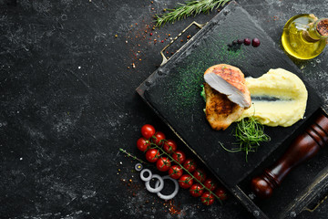 Baked chicken fillet with mashed potatoes on a black stone plate. Top view, free space for your text. Rustic style.