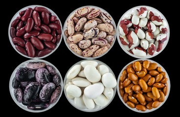 Six different varieties of beans in round glassware isolated on a black background.