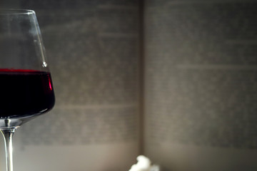 a glass of red wine in a beautiful vessel against the background of the text of an open book and a branch of white cotton close up