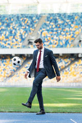young businessman in suit and glasses playing with soccer ball at stadium