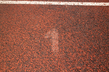 Almost non visible white number one, painted on the red tartan running track, on the outdoor sport...