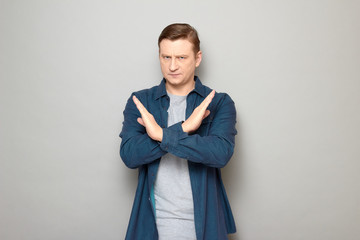 Portrait of serious man making cross with hands, showing stop gesture