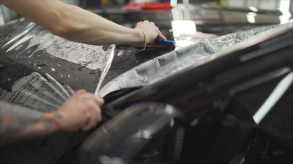 professional applying protective film to the red car. Master glues a protective film on the hood of the car