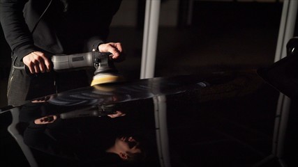 Car detailing - Hands with orbital polisher in auto repair shop. Polished black car.