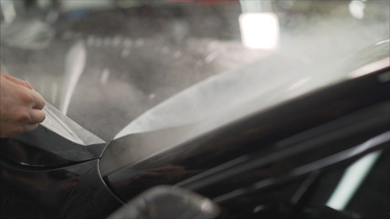 professional applying protective film to the red car. Master glues a protective film on the hood of...