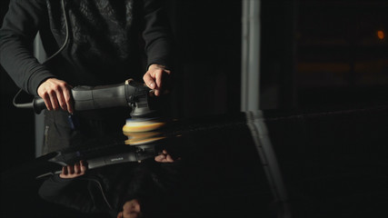 Fototapeta na wymiar Car detailing - Hands with orbital polisher in auto repair shop. Polished black car.