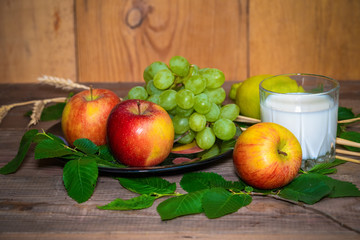 lemon, apples, green grapes, wheat and a glass with milk on a wooden table.
