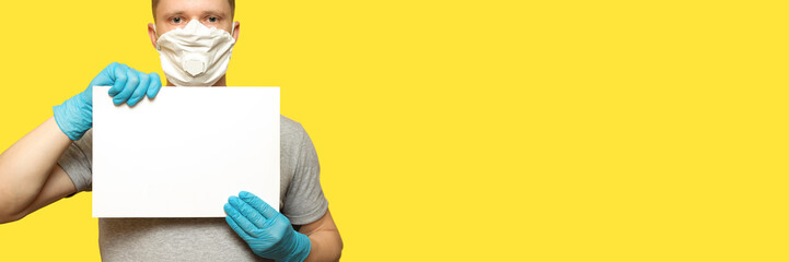Man in hygienic medical mask and blue gloves holding white poster. Mockup template. Advertising area for information. Coronavirus concept, COVID-19, copy Space.
