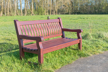 Brown wooden bench on the side of an abandoned path with a green meadow in the background