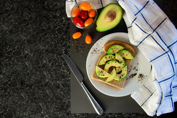 Wholesome brunch idea - avocado on wholemeal toast, sprinkled with black pepper, cherry tomatoes on the side, vegan healthy meal, home cooked and family friendly. Bright colours, contrasty flat lay.