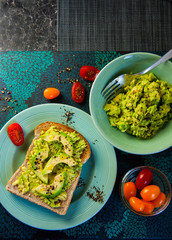 Wholesome brunch idea - avocado on wholemeal toast, sprinkled with black pepper, cherry tomatoes on the side, vegan healthy meal, home cooked and family friendly. Bright colours, contrasty flat lay.