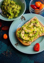 Wholesome brunch idea - avocado on wholemeal toast, sprinkled with black pepper, cherry tomatoes on the side, vegan healthy meal, home cooked and family friendly. Bright colours, contrasty flat lay.
