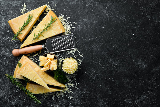Parmesan. Pieces of Parmesan cheese on black stone background. Top view. Free space for your text.