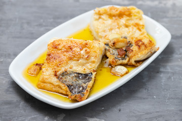 fried cofish with garlic and olive oil on white dish on ceramic background