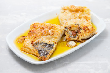 fried cofish with garlic and olive oil on white dish on ceramic background