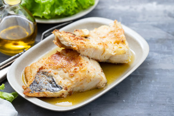 fried cofish with garlic and olive oil on white dish on ceramic background