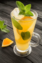 Orange drink or lemonade with mint and ice  in the glass  on the black wooden background. Closeup. Location vertical.