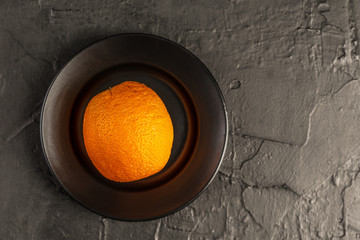 a whole orange orange on a smooth black plate and a textured black background
