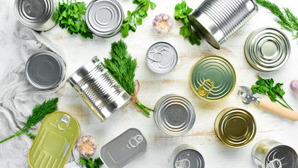 Canned food in tin jars on white wooden background. Top view.