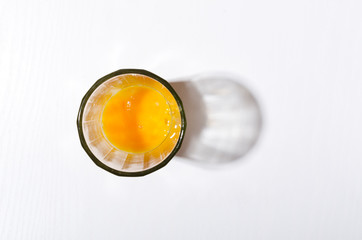 Top view of glass cup and fresh broken egg yolks in it on the white kitchen table.Empty space