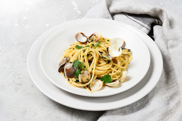 Traditional italian food seafood pasta with clams and parsley Spaghetti alle Vongole in white plates on a grey background. top view