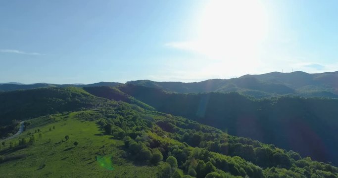 Aerial shot of woods, green hills and meadows under bright shining sun and blue sky