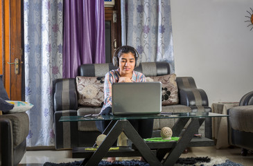 Obraz premium Young Indian girl is doing online study from home during lockdown by using laptop and headphone