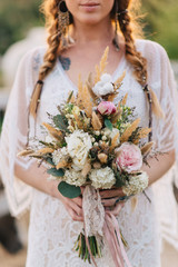 Boho style young bride holding a wedding bouquet in her hands, cropped shot. Close-up.
