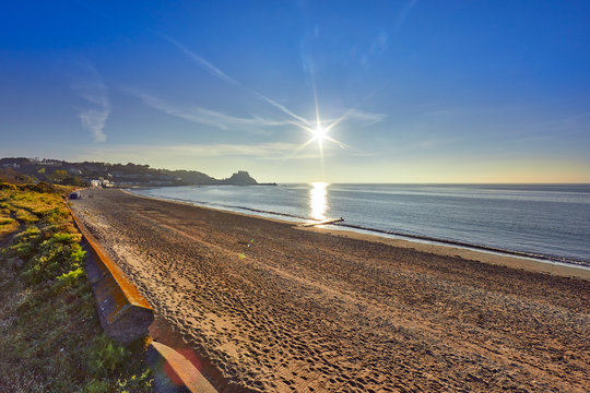 Image of Grouville bay with Gorey Castle in the background with a smooth sea at sunrise with the beach and blue sky. Jersey, Channel Islands, UK
