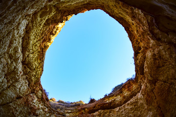 Portimao / Algarve, Portugal - A brown hole overlooking a blue sky in a rock formation on Praia da Rocha beach, sandstone in the summer during the daytime.