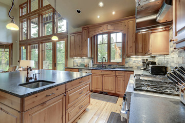 Large luxury kitchen interior with light wood hardwood floor and dark granite slab on island with huge windows.