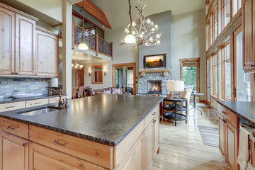 Large luxury wooden kitchen interior with light wood hardwood floor and dark granite slab on island...