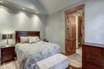 Bedroom interior with grey plaster venetian wall finish and cow skin on the floor. Luxury home with vaulted ceiling and dark rich wooden furniture.
