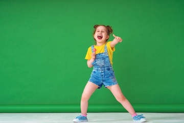 funny child shows gesture of approval,with a Lollipop on a stick out her tongue.