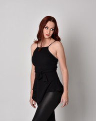 Fototapeta premium 3/4 portrait of a pretty girl with red hair wearing black leather pants and top. isolated against a studio background