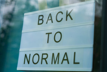 Back to normal sign hanging from a store window after Coronavirus Covid-19 lockdown measures are...