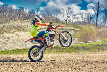 Motocross, a rider stands on the rear wheel of a bike, Riding on the rear wheel. Extreme, industrial, motorcycle cross-country riding for extreme.