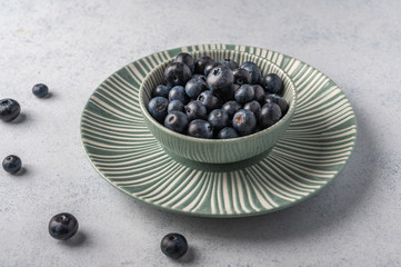 Blueberries into bowl on a plate on a light wooden background. Top view. Copy space for text