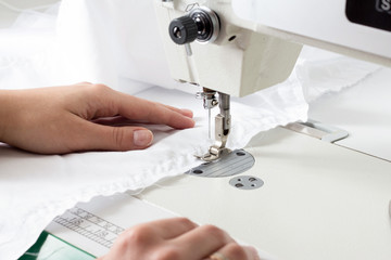 in the atelier of a sewing workshop, a young girl sews a dress on an overlock. hands hold the fabric and stitch the details.