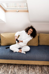Fototapeta premium KYIV, UKRAINE - APRIL 15, 2020: cheerful african american girl playing video game at home