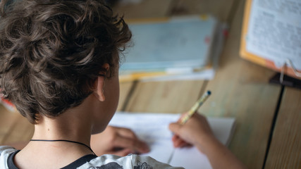 Close-up back view of a boy doing homework while sitting at a Desk at home.