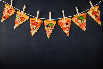 Pieces of pizza in the form of a garland of flags on a dark background. Pizza menu. Conceptual...