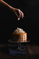 A woman prepares a cake with popcorn, salted caramel to stand on a wooden table on a dark background. Low key. Dark picture.